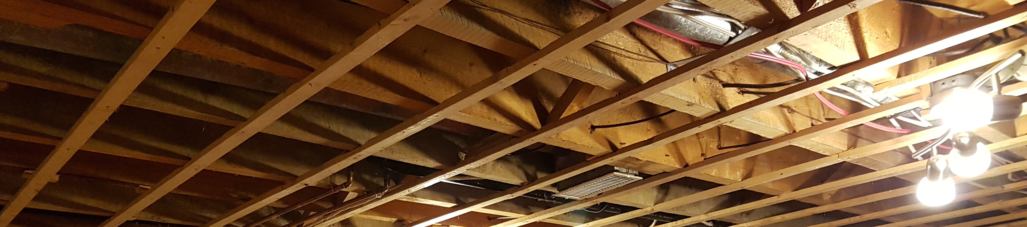 photo of an exposed basement ceiling with wires, wood strapping, and lights